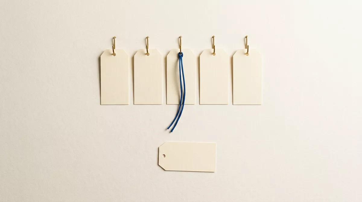 Five cream paper tags on brass hooks, a blue cord tied to the middle one, and a sixth tag lying unhooked below the row.